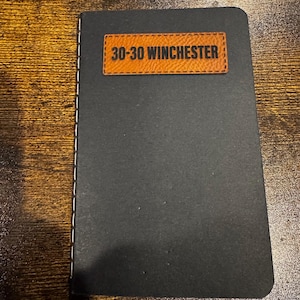 May include: A black notebook with a brown leather patch that says "30-30 Winchester".