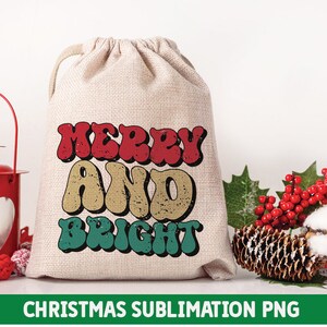 May include: A white canvas bag with a red, yellow, and green "Merry and Bright" design. The bag is sitting on a white surface with a red lantern, pine cones, and red berries.