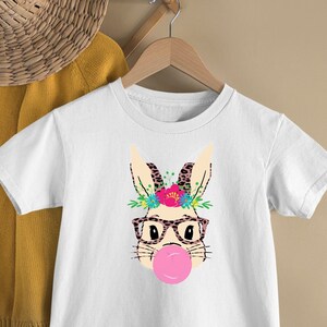 May include: White t-shirt with a graphic of a bunny wearing glasses and a flower crown, blowing a pink bubble.