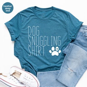 May include: A teal blue t-shirt with the text "DOG SNUGGLING SHIRT" in white with a white paw print with a small red heart in the center.