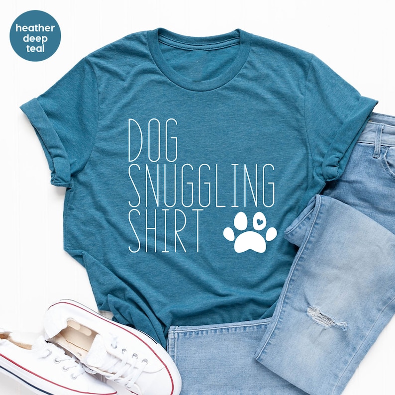 May include: A teal blue t-shirt with the text "DOG SNUGGLING SHIRT" in white with a white paw print with a small red heart in the center.