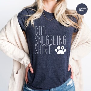 May include: A heather navy blue t-shirt with the text "DOG SNUGGLING SHIRT" and a white paw print with a small heart in the center.