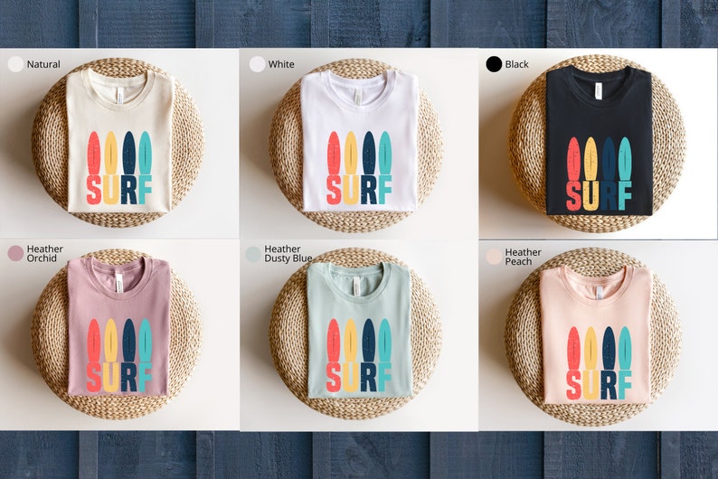 May include: A set of ten t-shirts in various colors featuring a graphic of colorful surfboards with the word "SURF" printed below. The t-shirts are displayed on a wooden background.