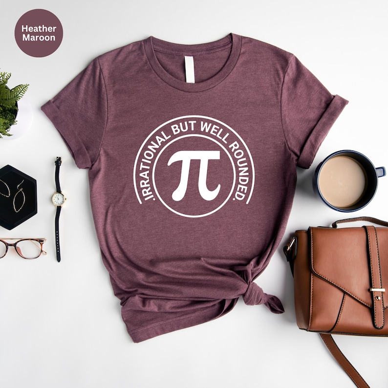 May include: Heather maroon t-shirt with a white circle graphic that says "Irrational but well rounded" and has a white pi symbol inside the circle.
