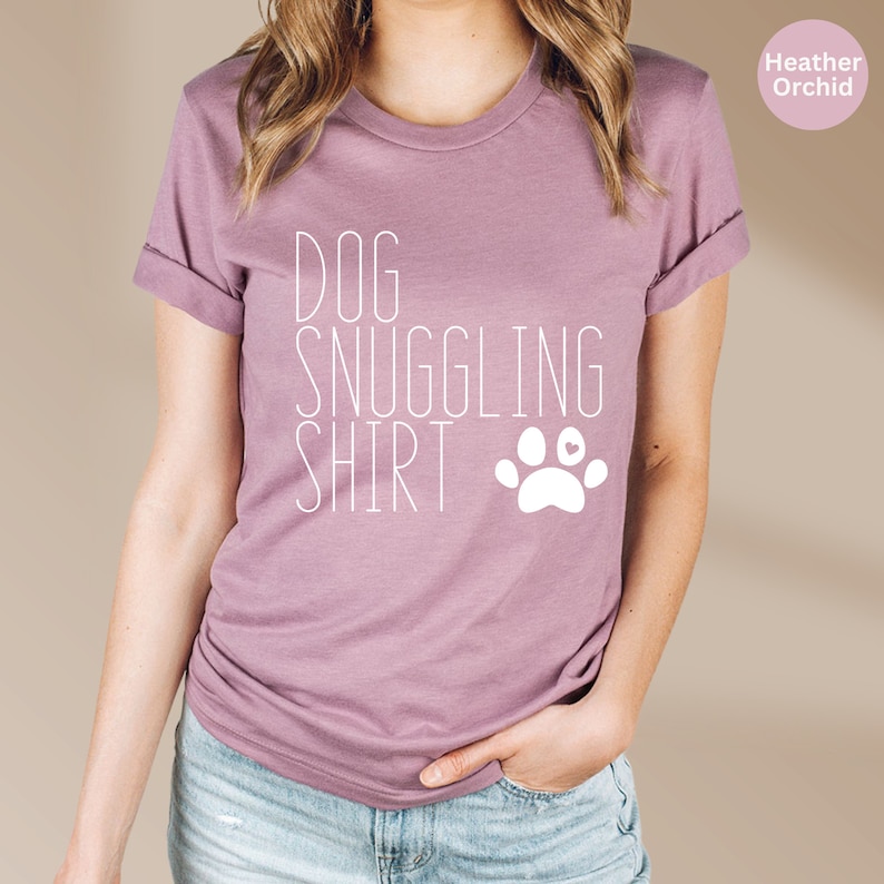 May include: A heather orchid t-shirt with the text "DOG SNUGGLING SHIRT" and a white paw print with a pink heart in the center.
