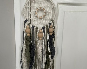 May include: A white dream catcher with a macrame design and wooden beads. The dream catcher has a fringe of white, green, and black yarn.