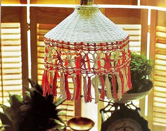 May include: A white crocheted lampshade with red and white fringe. The lampshade is hanging from a ceiling fixture and is surrounded by plants.