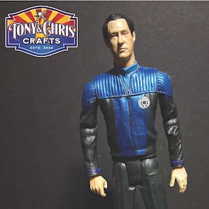 May include: A detailed action figure of a character in a blue and black uniform, standing on a circular base. The figure has a stern expression and is posed in a dynamic stance. The figure is from Tony & Chris Crafts.