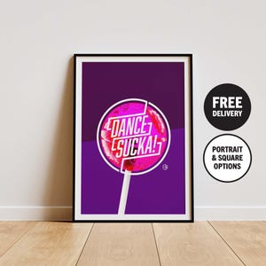 Op de afbeelding: Ingelijste kunstafdruk met een roze lolly met de witte tekst "DANCE SUCKA!". De lolly staat tegen een paarse achtergrond. De print zit in een zwarte lijst.