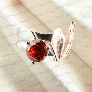 May include: A rose gold ring with a large, round, orange gemstone set in a prong setting. The ring has a unique, abstract design.