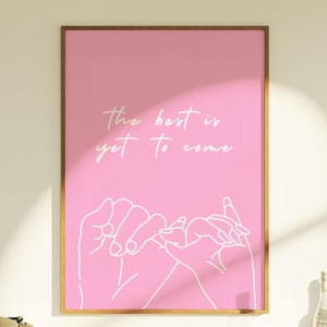 May include: Pink framed art print with the text "the best is yet to come" in white script. The print features a line drawing of two hands making a pinky promise. The frame is a light brown color.