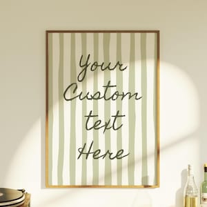 Puede incluir: Una impresión enmarcada con un borde dorado presenta un patrón de rayas verticales en verde claro y blanco roto. Las palabras "Your Custom text Here" están escritas en una fuente oscura, lo que la convierte en una obra de arte personalizable.