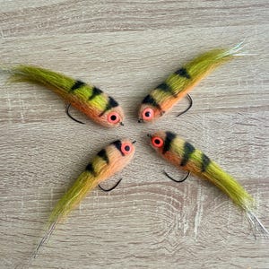 Peut inclure: Quatre leurres de pêche avec des rayures orange et noires et des plumes vertes et jaunes. Les leurres ont des yeux orange.