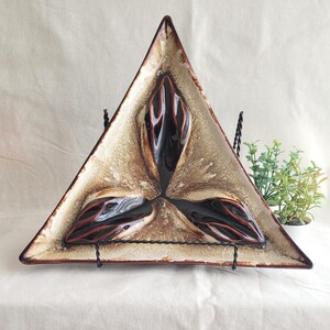 May include: Triangular ceramic serving dish. The dish has a brown and beige colour scheme with dark brown and red accents. It is supported by a black metal stand. A decorative and functional piece, ideal for serving.