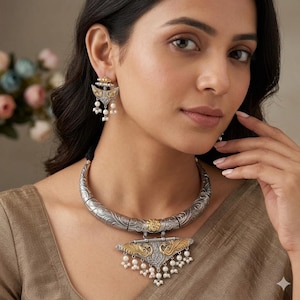 Puede incluir: Juego de collar y pendientes plateados y dorados. El collar presenta una banda plateada curva y grabada con un colgante dorado. El colgante tiene un diseño de pavo real y está adornado con pequeñas perlas blancas. Los pendientes reflejan el diseño del colgante.