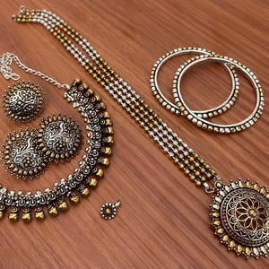 May include: An antique-style jewelry set featuring a necklace, earrings, a pendant, and two bangles. The set has silver and gold-tone accents. The necklace and earrings have a floral design. The jewelry is displayed on a wooden surface.