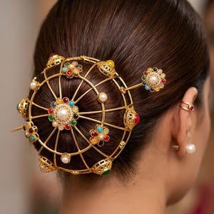 May include: A gold hair accessory with a circular design, decorated with colourful gemstones and pearls. The intricate piece is worn in the hair, showcasing a blend of elegance and artistry. The accessory features a central pearl and radial spokes.