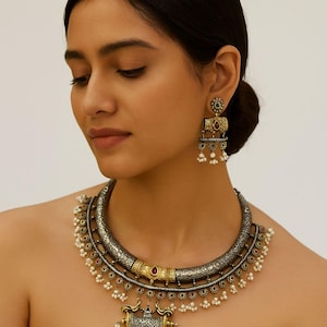 Puede incluir: Un collar y pendientes a juego de plata y oro ornamentados. El collar presenta un diseño detallado con detalles rojos y verdes, y pequeñas perlas blancas. Los pendientes tienen un diseño similar con piedras rojas y verdes.