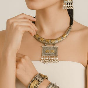 May include: A silver and gold-toned jewellery set with elephant motifs. The set includes a necklace, earrings, and two bracelets. The necklace and earrings have pearl accents. The bracelets are hinged and have detailed elephant designs.
