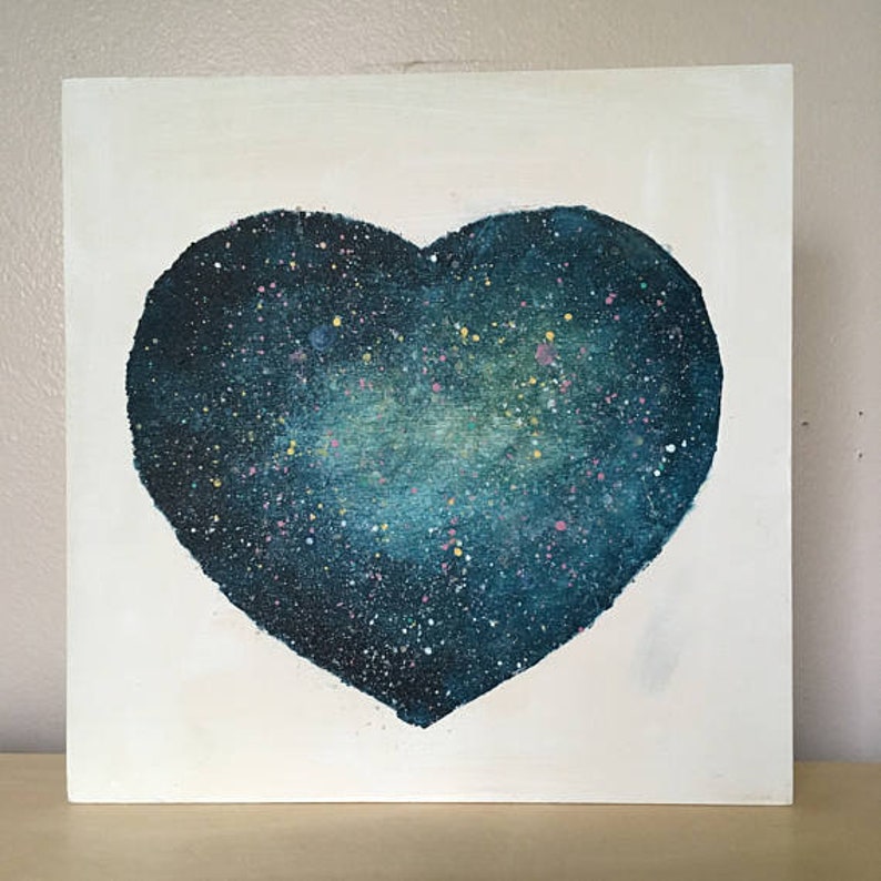 May include: A dark blue heart-shaped painting with a galaxy-like design. The heart is painted on a white canvas and has a speckled texture.