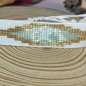May include: White beaded bracelet with a green and gold geometric pattern.