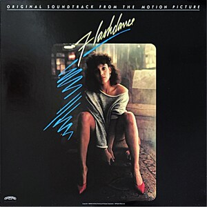 May include: Album cover for the "Flashdance" soundtrack. The cover features a woman in a gray sweatshirt and red heels, with the title in a stylized font and blue lines. The text at the top reads "Original Soundtrack From The Motion Picture."