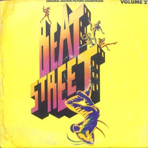 May include: Album cover for the "Beat Street" original motion picture soundtrack, Volume 2. The cover features the title in large, stylized, orange and pink letters against a yellow background. Silhouettes of breakdancers are on the cover.