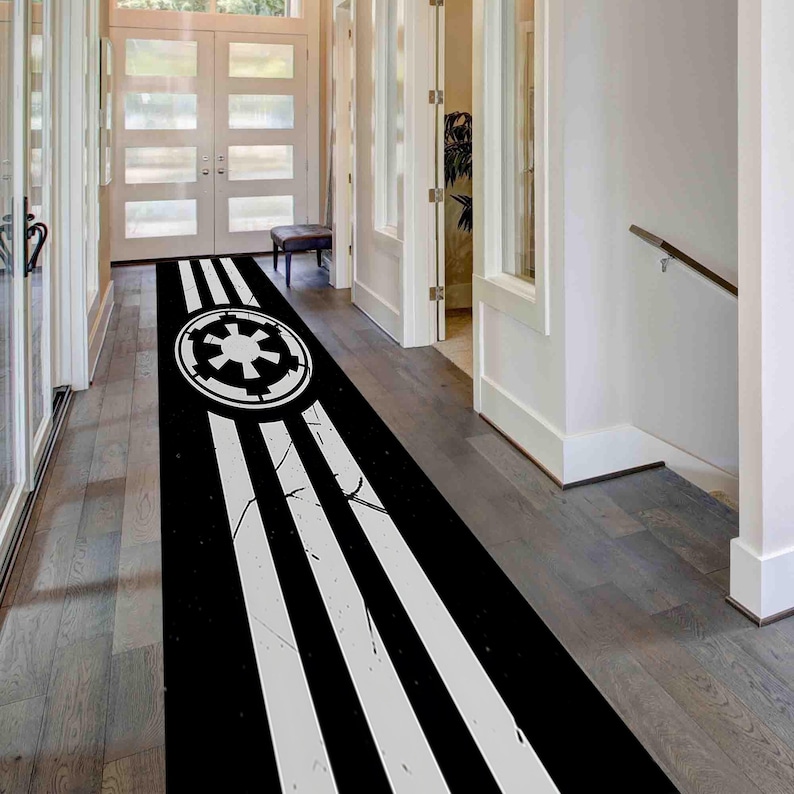 May include: Black and white hallway runner rug featuring a circular emblem and three white stripes. The rug has a distressed design and is placed in a hallway with wooden flooring and white doors.
