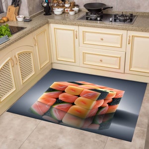 Op de afbeelding: Een keukenkleed met een 3D-ontwerp van een kubus gemaakt van sushi. De sushi is gemaakt van zalm, avocado en zwarte sesamzaadjes. Het kleed ligt op een betegelde vloer.