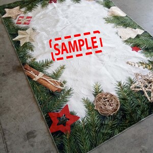 May include: Rectangular Christmas-themed table runner with a white center and a border of green pine needles. The border is decorated with red stars, gold stars, ornaments, and cinnamon sticks. The word "SAMPLE" is printed in red.