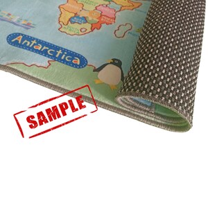 May include: A rolled-up children's rug featuring a world map design with continents and oceans in various colors. The word "Antarctica" is visible, along with a cartoon penguin. The rug has a gray border and a non-slip backing. The word "SAMPLE" is stamped on the rug.