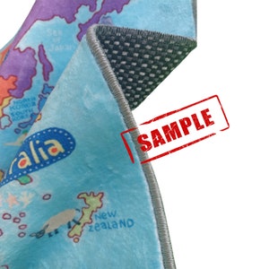 May include: A section of a light blue map-themed rug with a world map design. The rug has a gray border and a non-slip backing. The word "SAMPLE" is stamped in red on the rug.