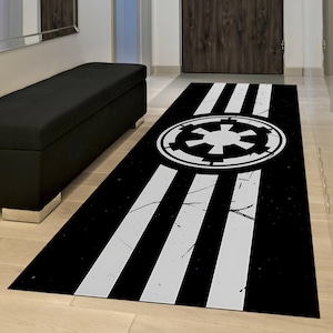 May include: Black and white rectangular rug featuring a central emblem and three white stripes. The emblem is a white circular design with a starburst pattern. The rug has a distressed, vintage look.