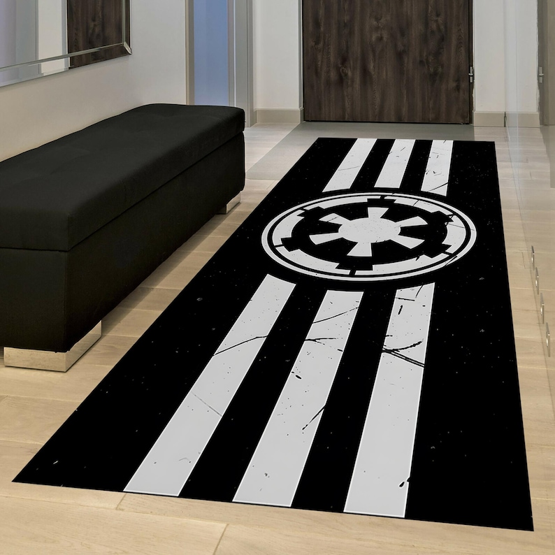 May include: Black and white rectangular rug featuring a central emblem and three white stripes. The emblem is a white circular design with a starburst pattern. The rug has a distressed, vintage look.