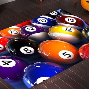 May include: A colorful rug with a billiard ball design. The rug features a variety of billiard balls with different numbers, including 1, 4, 5, 8, 9, 10, 11, 12, 13, 15, and 6. The balls are arranged in a random pattern on a blue background.