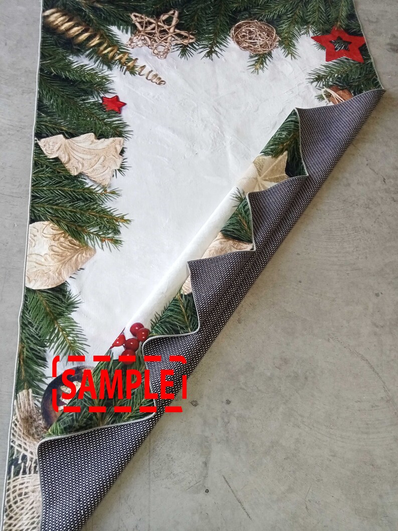 May include: A Christmas-themed table runner with a white center and a border of green pine branches, red stars, and gold ornaments. The reverse side is a dark gray with a dotted pattern. The word "SAMPLE" is visible.