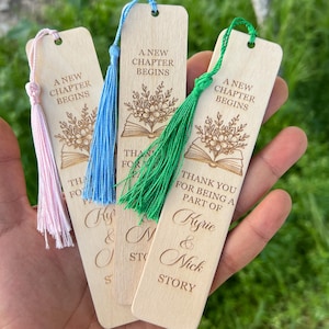 Pode incluir: Marcadores de livros de madeira com borlas coloridas. Cada marcador tem o texto "A New Chapter Begins" e "Thank you for being a part of Kyrie & Nick Story". Os marcadores s&atilde;o castanhos claros com borlas rosa, azuis e verdes.