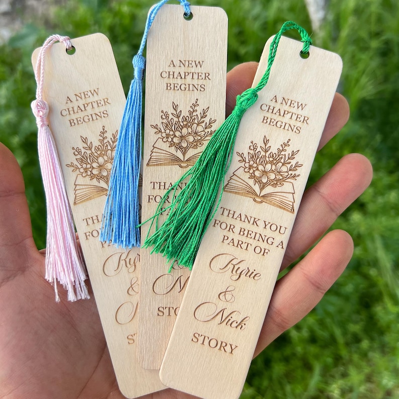 Pode incluir: Marcadores de livros de madeira com borlas coloridas. Cada marcador tem o texto "A New Chapter Begins" e "Thank you for being a part of Kyrie & Nick Story". Os marcadores s&atilde;o castanhos claros com borlas rosa, azuis e verdes.