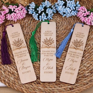 Pode incluir: Tr&ecirc;s marcadores de livros de madeira com borlas. Cada marcador de livros tem o texto "A NEW CHAPTER BEGINS" e "THANK YOU FOR BEING A PART OF" seguido de nomes e a palavra "STORY". Os marcadores de livros t&ecirc;m desenhos florais e de livros.