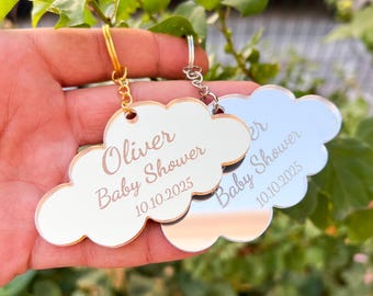 Puede incluir: Dos llaveros de plata en forma de nube con el texto "Oliver Baby Shower 10.10.2025" y "Baby Shower 10.10.2025" grabado en ellos.