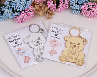 May include: Two silver and gold keychains with a bear design. The keychains are packaged in clear plastic bags with a white card that says "Alicia's Baby Shower 06/09/2028".