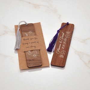 May include: Wooden bookmarks with floral designs and tassels. One bookmark is paired with a kraft paper card that reads "Thank you for being a part of our story." The other bookmark has the names "Arienne & Daniel" and the date "10.10.2029".