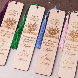 Pode incluir: Marcadores de livros de madeira com desenhos florais e de livros gravados, com o texto "A New Chapter Begins" e nomes personalizados. Cada marcador tem uma borla colorida, com op&ccedil;&otilde;es roxas, verdes, azuis e rosas.