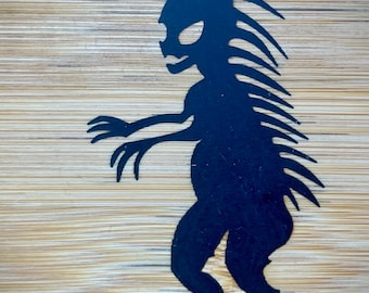May include: Black silhouette of a creature with spiky hair and claws, standing on a wood background.