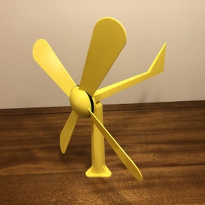 May include: A yellow plastic wind turbine with four blades. The turbine is mounted on a yellow plastic base.