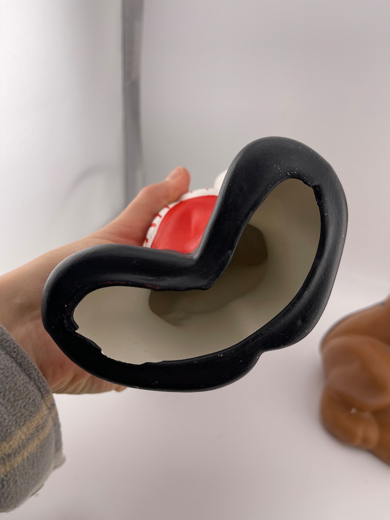 Puede incluir: Una figura de cer&aacute;mica de Pap&aacute; Noel con un gorro rojo y barba blanca. La figura lleva un saco y tiene una base negra.