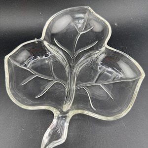 Puede incluir: Plato para servir de vidrio transparente en forma de hoja. El plato tiene tres secciones principales, con un tallo central y detalles de venas. Los bordes son ligeramente redondeados. El plato está diseñado para parecerse a una hoja.