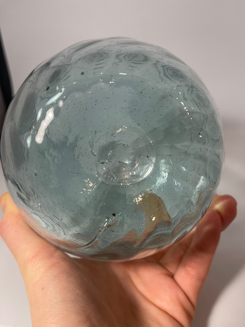 May include: A round, light blue glass float with a textured surface. The float has a small hole at the bottom.
