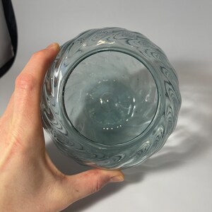 May include: A clear glass vase with a wavy, textured design. The vase is empty and has a round shape.