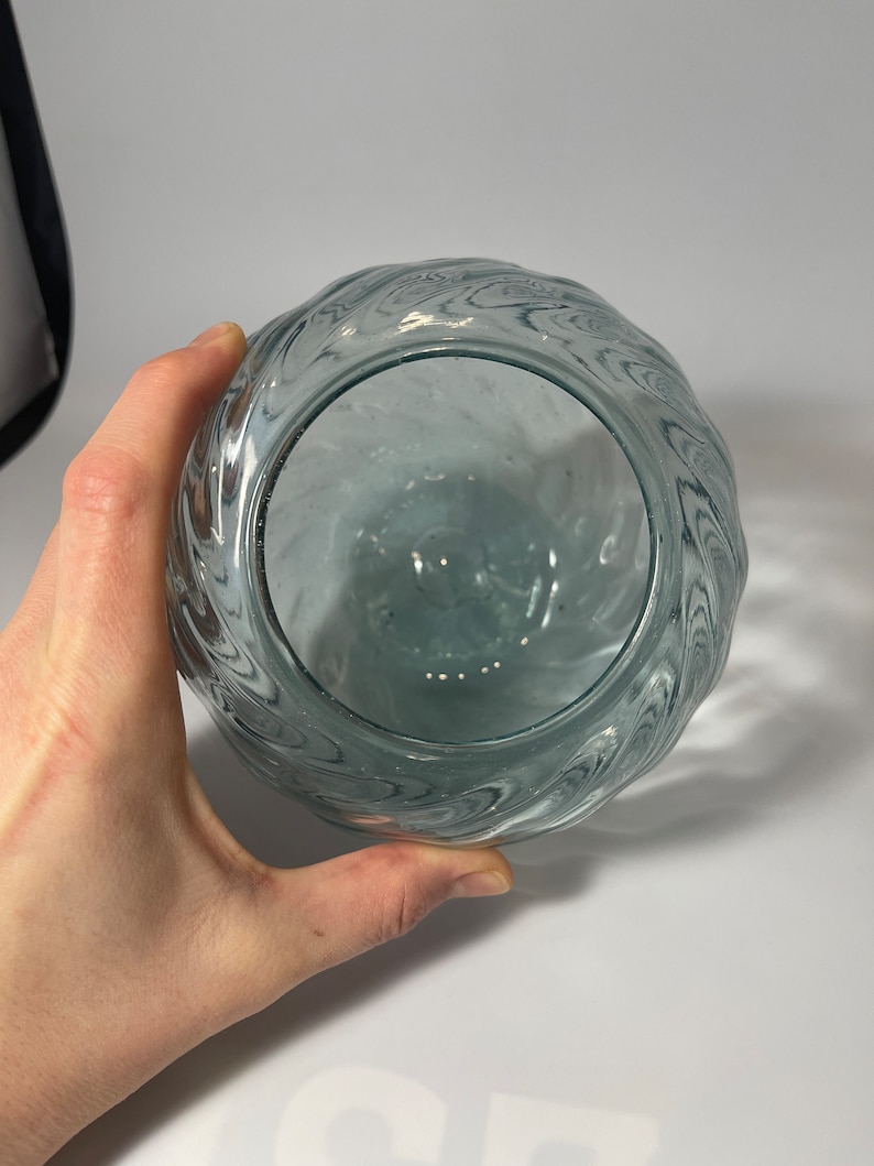May include: A clear glass vase with a wavy, textured design. The vase is empty and has a round shape.